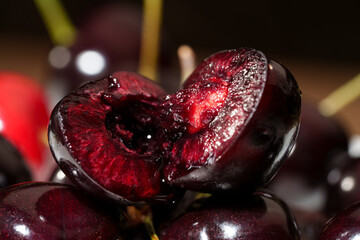 Close-up of sliced dark red cherry with glossy juicy flesh, visible pit cavity, rich texture, and dramatic low light macro detail against dark background for fresh food and dessert use © Edita