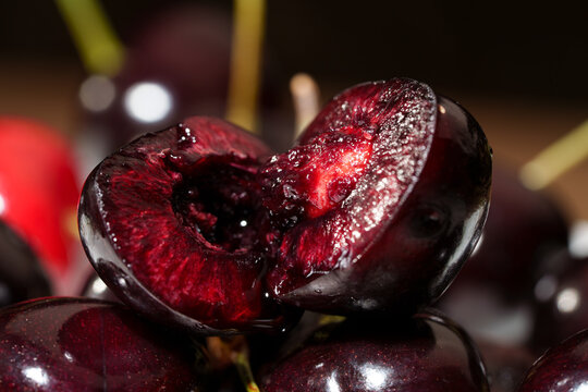 Close-up of sliced dark red cherry with glossy juicy flesh, visible pit cavity, rich texture, and dramatic low light macro detail against dark background for fresh food and dessert use