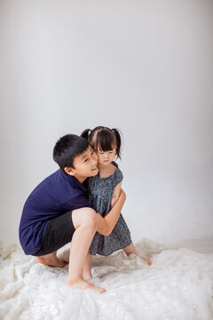 An Asian boy is holding a little girl and playing indoors.