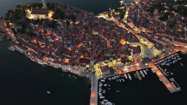 Aerial view of the historic old town of Rovinj illuminated at night with boats docked in the harbor, Rovinj, Istria County, Croatia.