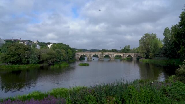 Vista general del puente romano de Lugo en un d&iacute;a nublado, sobre el r&iacute;o Mi&ntilde;o, mostrando su estructura hist&oacute;rica y el paisaje gallego.