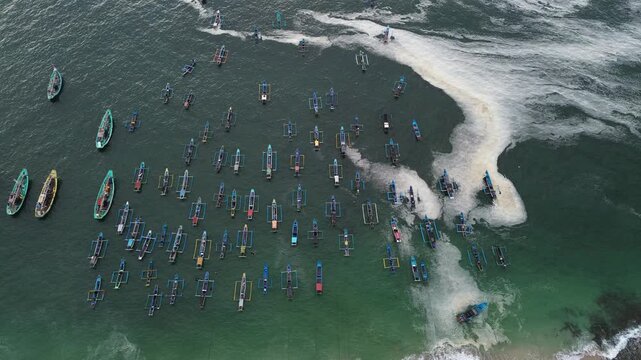 Aerial view of numerous traditional fishing boats anchored in the turquoise waters off the coast of Papuma Beach in East Java, Indonesia.