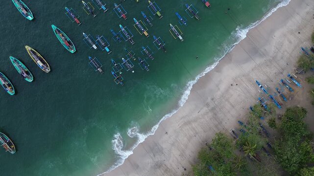 Aerial view of traditional fishing boats anchored in the turquoise waters of Papuma Beach, East Java, Indonesia.
