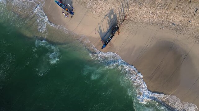 Aerial view of a traditional wooden boat on the sandy shore of Papuma Beach with turquoise waves crashing against the coastline in East Java, Indonesia.