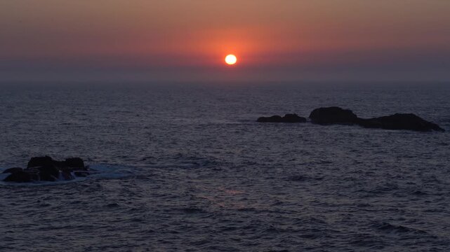 Atardecer atl&aacute;ntico desde la costa de A Coru&ntilde;a, con el sol naranja a punto de ponerse sobre el horizonte y ti&ntilde;endo el mar de tonos c&aacute;lidos.
