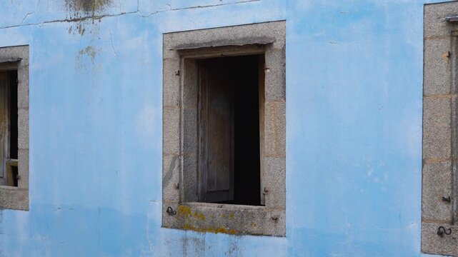 Detalle de una ventana de una casa abandonada en el casco antiguo de Lugo, con fachada azul envejecida y puertas de madera abiertas que acent&uacute;an su aspecto decadente.