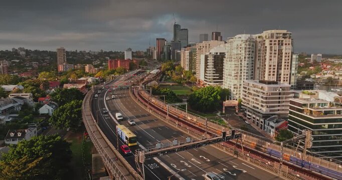 Aerial drone footage capturing the busy city of Sydney Australia, multiple lanes of traffic flowing on a major elevated highway structure with a bustling skyline and urban landscape in evening light