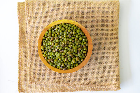 A bowl of fresh raw mung bean on burlap background. Green Gram (Vigna radiata) or whole green moong dal in a wooden bowl. Top view