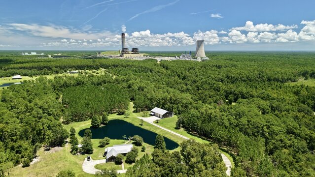 Aerial view of the Seminole Electric power plant with its cooling towers and chimneys rising above the surrounding dense forest and rural landscape in Palatka, Florida, United States.