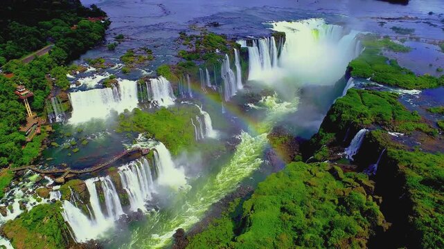 Stunning aerial footage showcasing powerful water cascades of Iguazu falls with vibrant rainbow appearing.