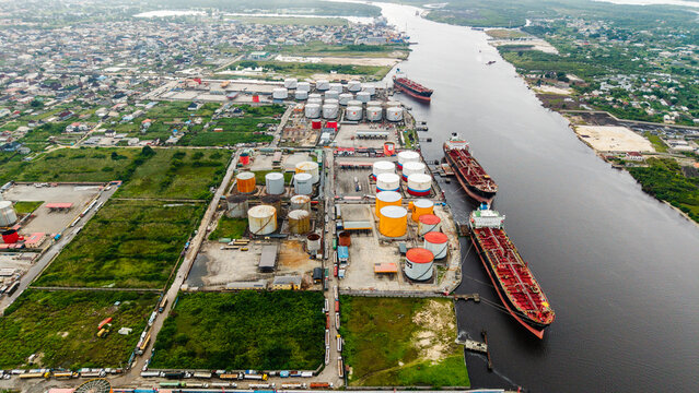 Aerial view of the industrial oil storage facility in Satellite Town with large storage tanks and cargo ships docked along the river in Lagos, Lagos, Nigeria.