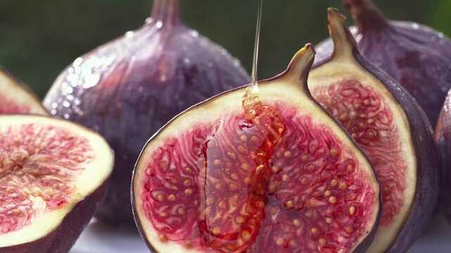 Macro close up shot of golden honey dripping down onto a freshly cut halved purple fig fruit healthy sweet dessert backdrop