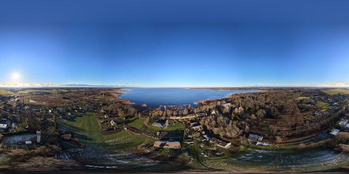 Aerial view of Lake Burtnieks surrounded by rural fields, forests, and small settlements under a clear blue sky in Burtnieki, Valmiera Municipality, Latvia.