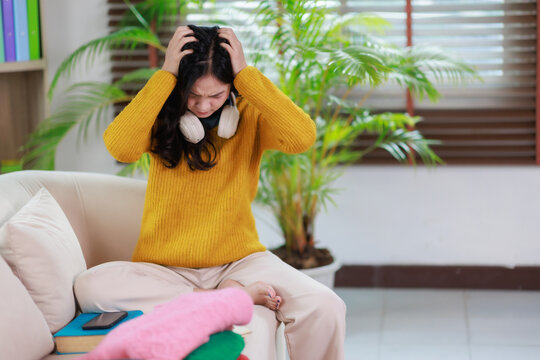 Young frustrated woman feeling stressed and overwhelmed with a severe headache. Sitting on a sofa at home. Grappling with mental health issues. Exhaustion