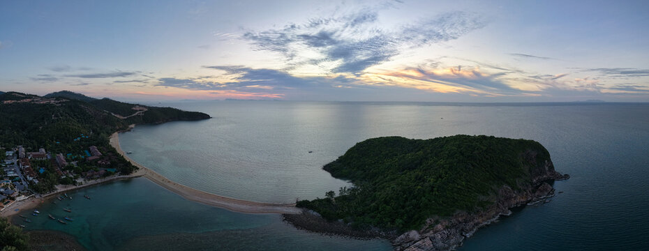 Aerial view of the sandbar connecting to Ko Pha Ngan island at sunset with calm sea, lush tropical vegetation, and colorful clouds in Ko Pha-ngan District, Surat Thani, Thailand.