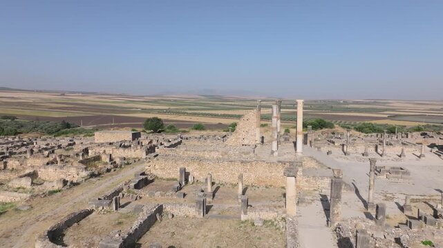 Drone aerial view of the Capitol within the UNESCO World Heritage-listed Volubilis Archaeological Site in Morocco, revealing the surrounding Roman urban landscape and fertile plains.