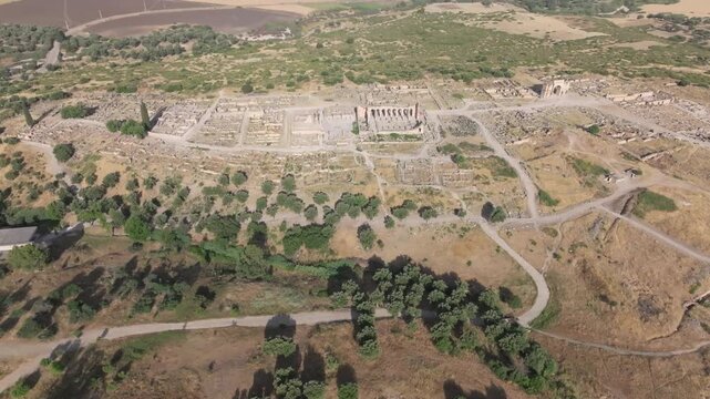 High-altitude drone view of the UNESCO World Heritage-listed Volubilis Archaeological Site in Morocco, revealing the ancient Roman city, surrounding olive groves, fertile valleys, and historic landsca