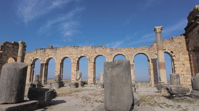 Ground-level view of the Roman Basilica arcade at the UNESCO-listed Volubilis Archaeological Site in Morocco, featuring monumental stone arches, columns, and preserved architectural remains.