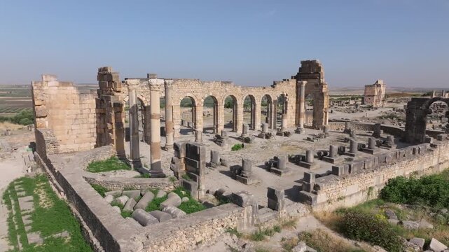 Low-altitude oblique drone view of the Roman Basilica at the UNESCO World Heritage-listed Volubilis Archaeological Site in Morocco, highlighting its monumental arcade and preserved civic architecture.