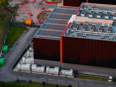 Aerial view of a modern datacenter with rooftop cooling units and ground-level infrastructure, surrounded by paved areas and greenery in Settecamini, Lazio, Italy.