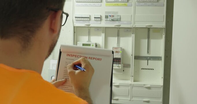 Technician completing an electrical inspection report in front of an electrical distribution panel, documenting inspection results, safety checks, and maintenance records.