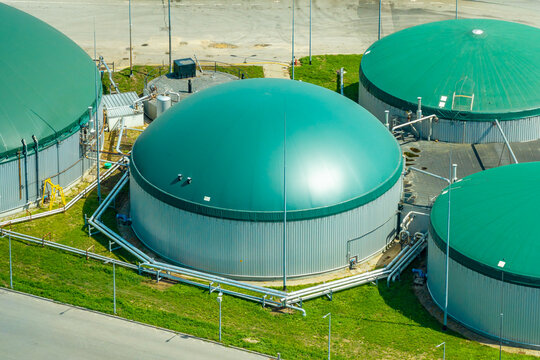 Aerial view of a biogas plant featuring large green domed storage tanks for fermented mass, connected by industrial metal piping, situated in Poland.