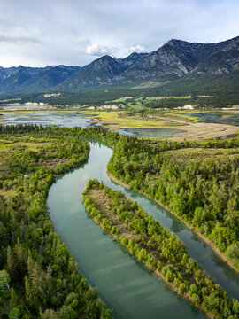 Aerial view of Radium Wetlands Recreation Site with a winding river flowing through lush forests and wetlands against majestic mountains in East Kootenay, British Columbia, Canada.