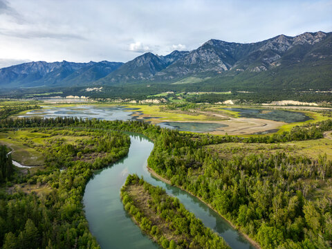 Aerial view of Radium Wetlands Recreation Site with a winding river through lush green wetlands and forests, set against mountains in East Kootenay, British Columbia, Canada.
