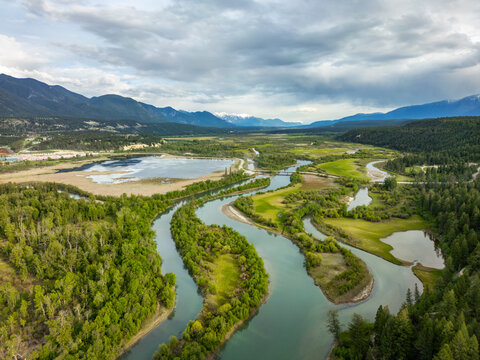 Aerial view of Radium Wetlands Recreation Site featuring a winding river through lush meadows and forests with distant mountains, East Kootenay, British Columbia, Canada.