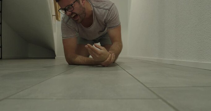 Slow-motion shot of a man falling indoors and injuring or spraining his wrist while trying to catch himself, illustrating home accidents and wrist injuries.