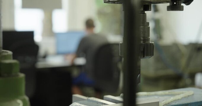 Close-up of a CNC milling machine in the foreground while an engineer works on a computer in the background, illustrating precision manufacturing and industrial production.