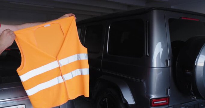 Person holding a high-visibility reflective safety vest next to a car, demonstrating mandatory emergency equipment for roadside breakdowns and traffic safety.