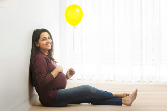 Pregnant woman sitting with a yellow balloon in hand and smiling. 
