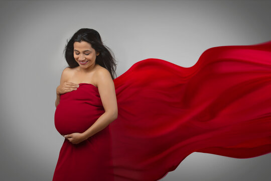 Pregnant woman with hands on her baby bump in a red dress. 