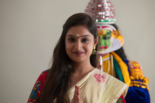 South indian woman in a welcoming gesture with a kathakali dancer in the back.