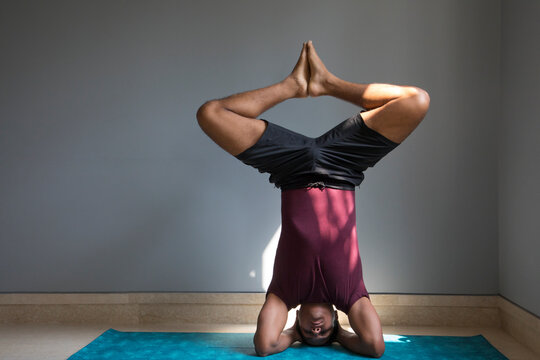 Man doing headstand on a yoga mat in his living room. 
