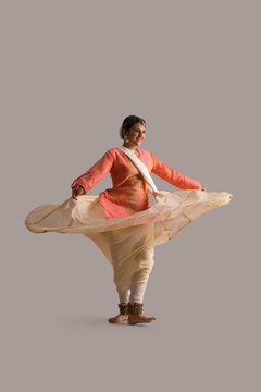 Gorgeous kathak dancer circling in front of a plain background and smiling.  