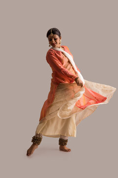 Beautiful kathak dancer performing gracefully over a plain background. 
