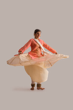 Gorgeous kathak dancer circling in front of a plain background and smiling.  