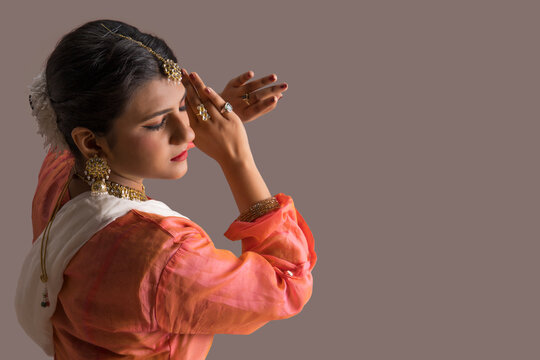 Beautiful kathak dancer performing through her expressions over a plain background. 