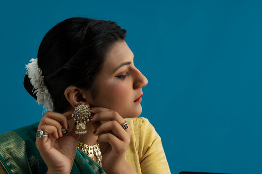 Kathak dancer wearing earrings in front of a blue background. 