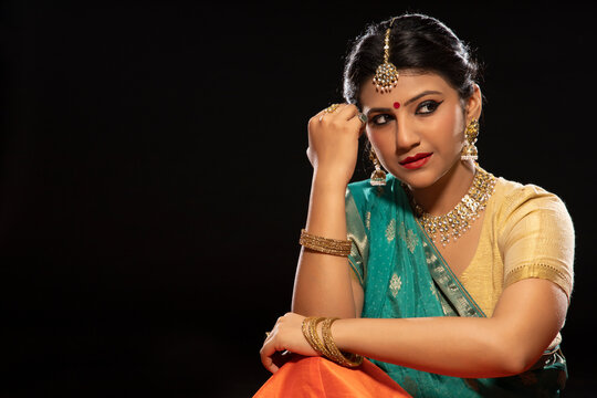Kathak dancer sitting gracefully in front of a dark background. 