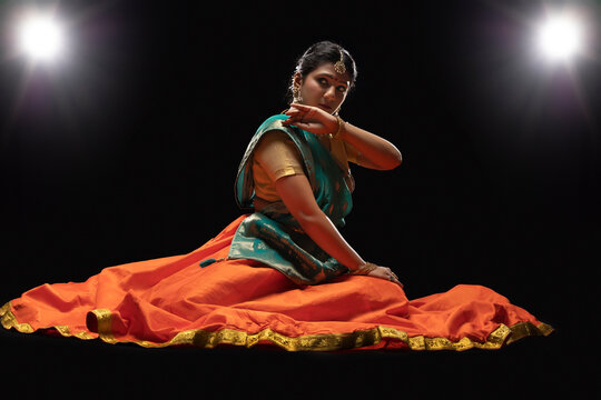 Kathak dancer sitting gracefully in front of a dark background. 