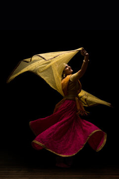 Kathak dancer circling gracefully during a performance in front of a dark background. 