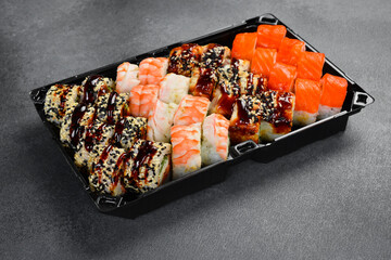 Assorted Japanese sushi rolls topped with fresh salmon shrimp unagi sauce and sesame seeds in takeaway tray. Gourmet seafood set. Tasty fresh Asian food. © Yaruniv-Studio