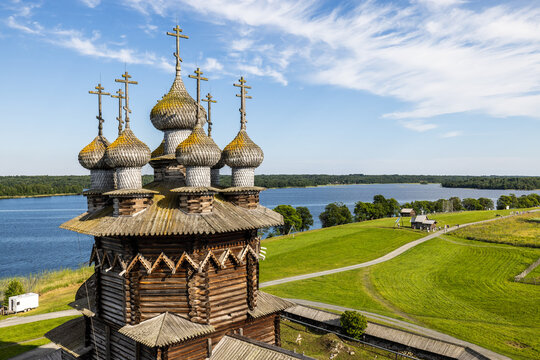 Aerial view of the historic wooden Kizhi Pogost church with its iconic onion domes, surrounded by lush green fields and the waters of Lake Onega in Petrozavodsk, Republic of Karelia, Russia.