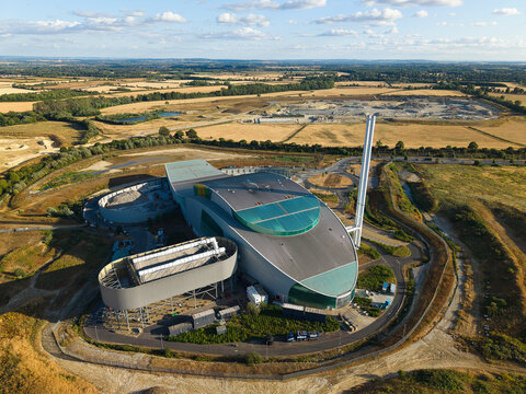Aerial view of the Energy Recovery Facility with modern architecture and tall chimney, situated amidst rural fields and open landscape in Bicester, England, United Kingdom.