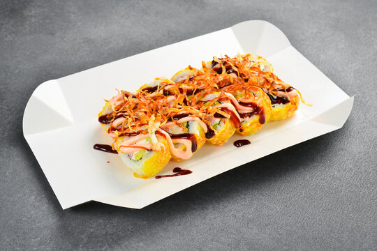 Hot tempura sushi roll set with avocado served on white takeaway tray. Tasty Japanese rolls topped with spicy mayonnaise and unagi sauce. Fresh gourmet food.