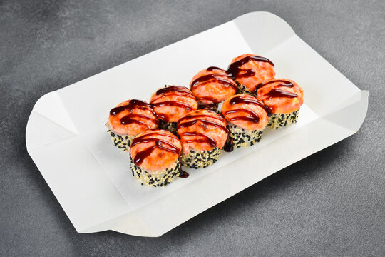 Delicious baked sushi roll set topped with creamy cheese and unagi sauce in takeaway box. Fresh Japanese rolls wrapped in nori. Tasty gourmet food.