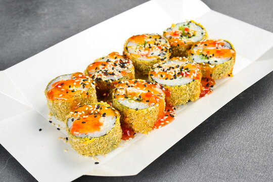 Crispy tempura sushi roll set topped with sweet chili sauce and sesame seeds in paper tray. Gourmet Japanese takeaway food. Fresh delicious seafood meal.